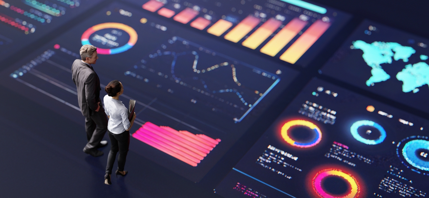 Two businesspeople stand on a dark floor displaying large, colorful digital graphs and charts—bar graphs, line charts, circular diagrams, and a world map—illustrating data analysis as one of the key Pillars of Successful Branding.