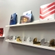 Two white wall shelves display magazines, brochures, and several silver and gold semicircular trophies or international design awards against a light gray wall.