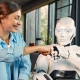 A smiling woman in a blue shirt fist bumps a white humanoid robot, showcasing the friendly side of Artificial Intelligence In Digital Marketing, while sitting indoors in a modern, sunlit room with large windows and blue curtains.