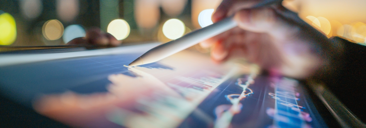 A hand uses a stylus to interact with colorful digital graphs on a tablet screen, illustrating branding strategy against a blurred cityscape and glowing lights in the background.