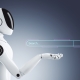 A humanoid robot with a white and black body holds its hand out under a floating digital search bar featuring the words Search... and a magnifying glass icon, symbolizing AI search optimization on a gradient gray background.